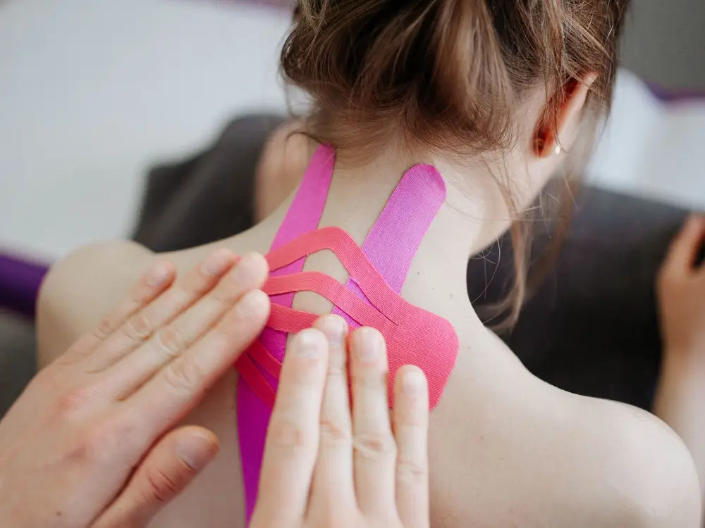 Therapeut brengt tape aan op de nek van een patiënt